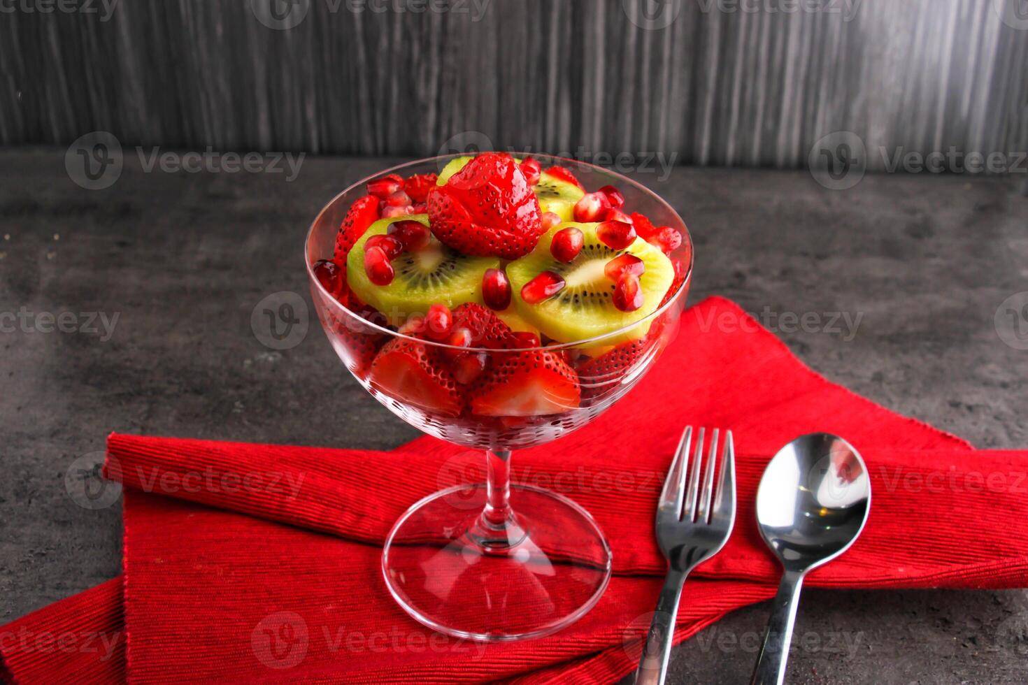 Colorful Fruit Salad with Strawberries, Kiwi, and Pomegranate Seeds served in bowl isolated on red napkin side view of healthy eating food on dark background photo