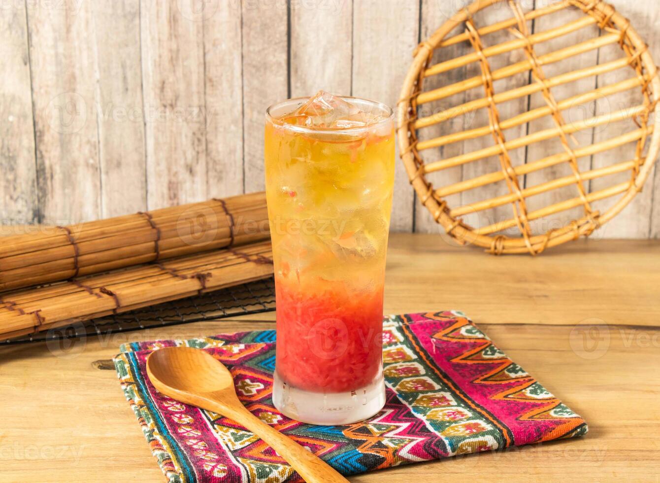 Spring Bud Grapefruit iced tea or Vibrant Layered Fruit Tea filled with ice cubes served in tall glass isolated on napkin side view on wooden table of taiwan drink photo