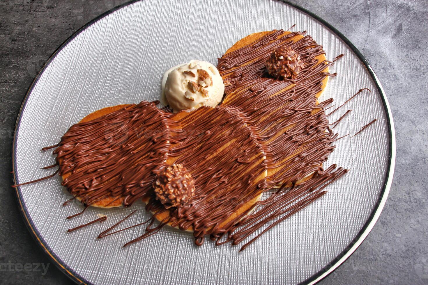 Chocolate Nutella Pancake Stack drizzled with rich chocolate sauce and topped with chocolate candy balls and vanilla ice cream served on a white plate in the background top view of dessert photo