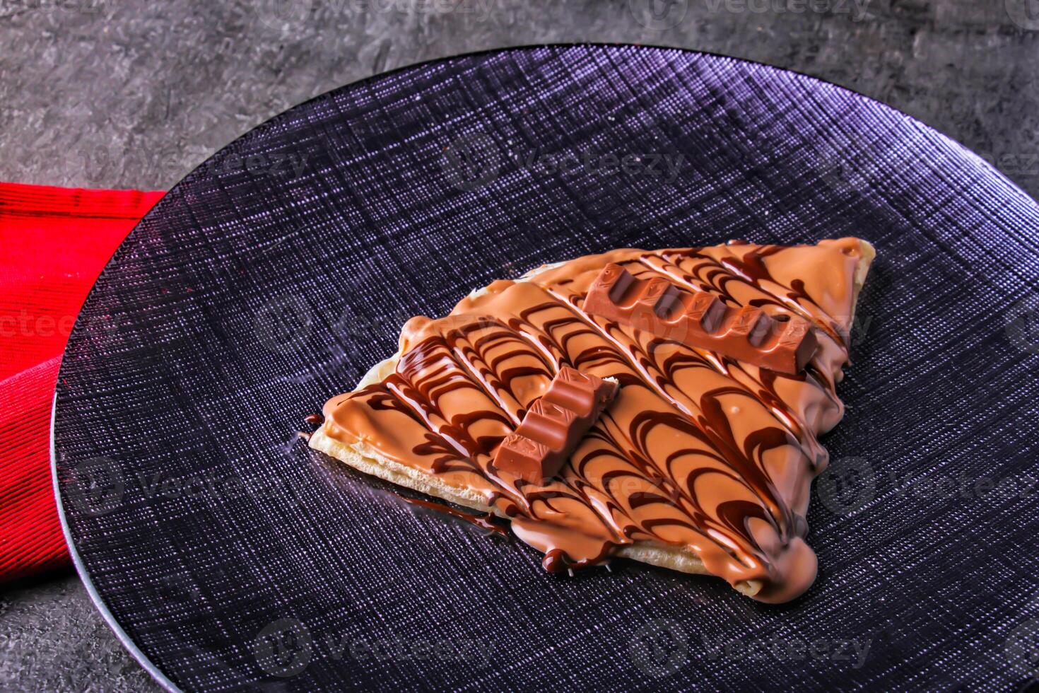 Decadent Kinder Chocolate Crepe topped with rich chocolate sauce and topped and chocolate chunks in plate isolated on table side view of indulgent dessert photo