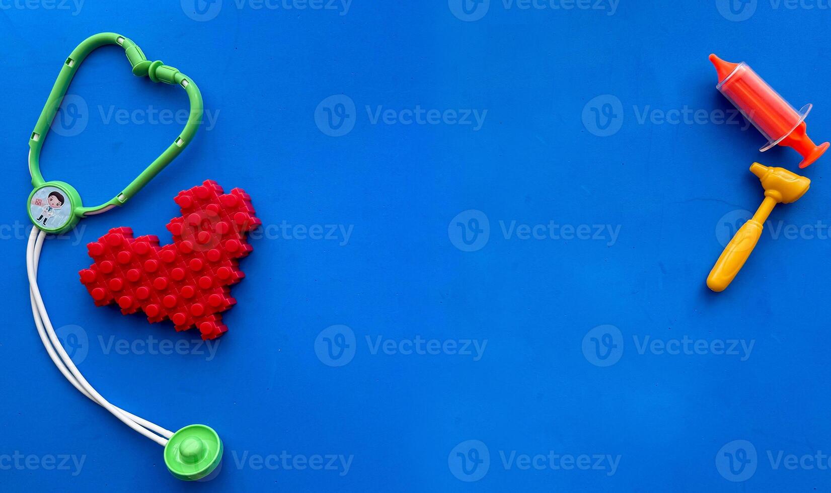 Set of toy medical equipment, syringe, injection, stethoscope, otoscope. Funny blue copy space background and heart shape from toy constructor. Healthy lifestyle concept. photo