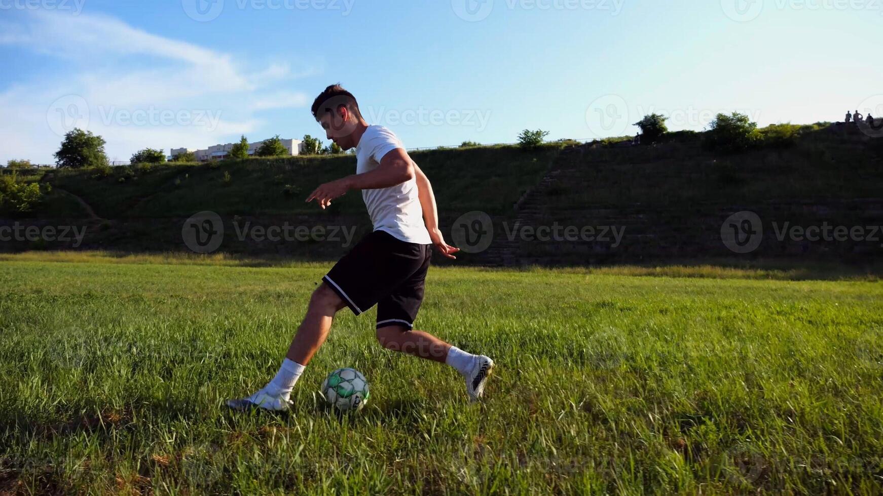 Professional footballer in uniform shows tricks with ball while running at green field. Sportsman kicks ball during jogging at meadow on sunny day. Young man training at stadium. Freestyle football photo