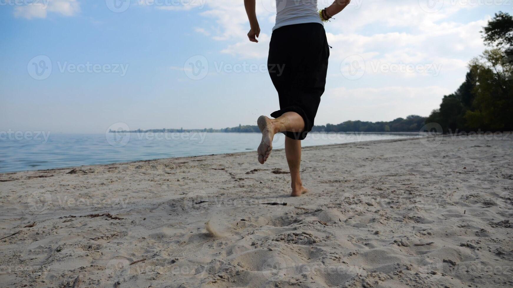 Bare feet of adult woman jogging on sand at the beach with seascape at background. Female legs running along sea shore. Happy lady spending time near ocean coast. Concept of summer vacation photo