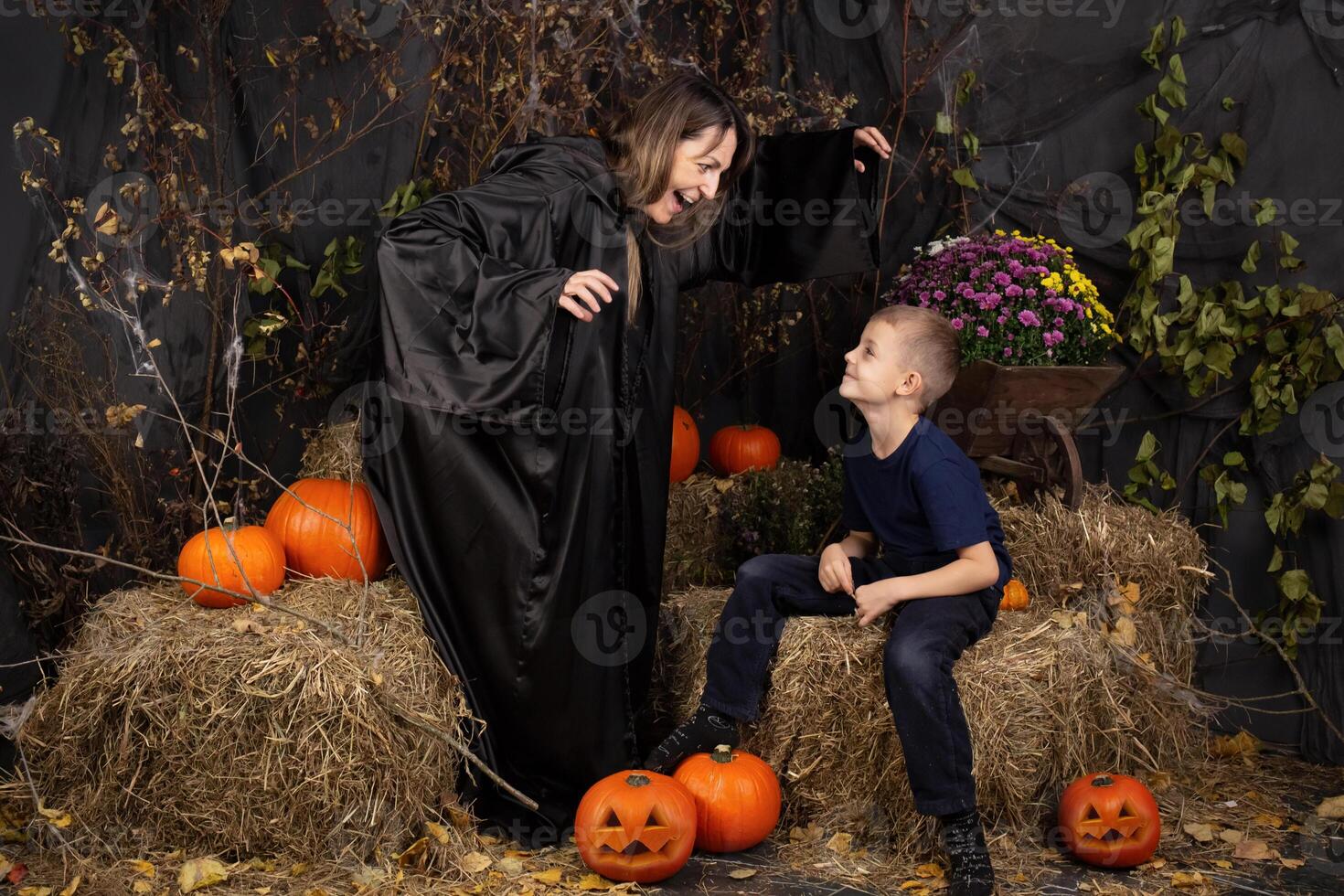 Happy mother and son playing during Halloween. cheerful family in carnival costumes in a room painted with pumpkins for the holiday of Halloween. Cheerful children playing with pumpkins and sweets. photo