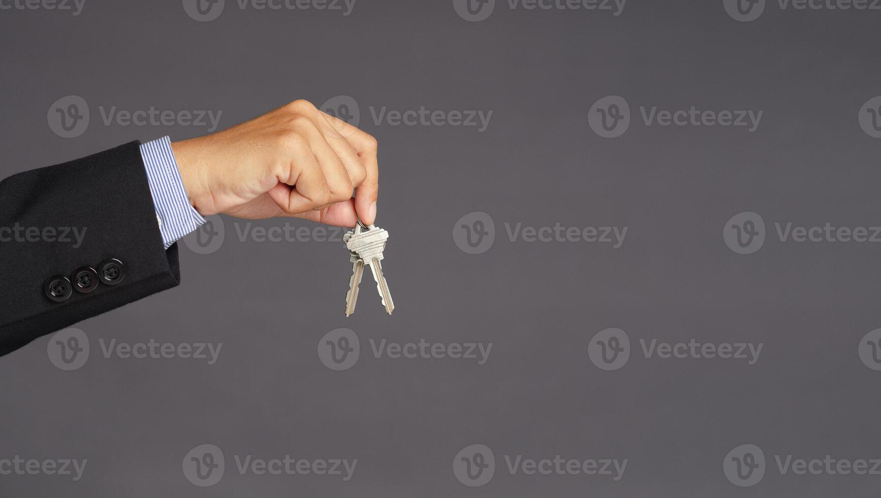A businessman's hand holds a bunch of two keys over gray background with blank copy space for text message or information content photo