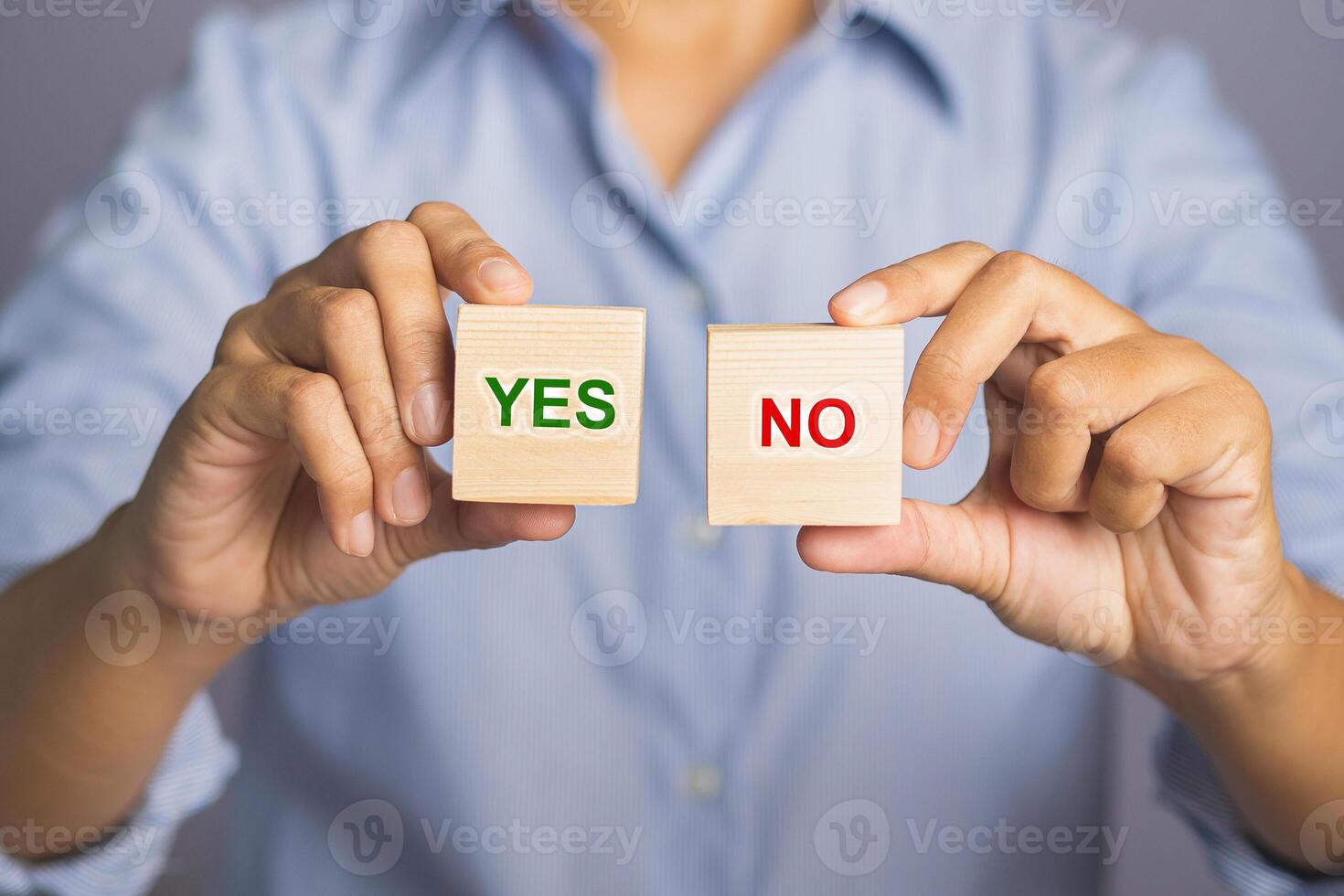 Choice yes or no on wooden cubes blocks concept. Hand of holding two wooden cubes with text yes and no for choice while standing with gray background in the studio. Close-up photo