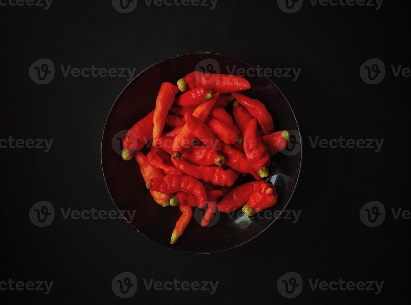 A bowl of red peppers on a black background. Top view photo