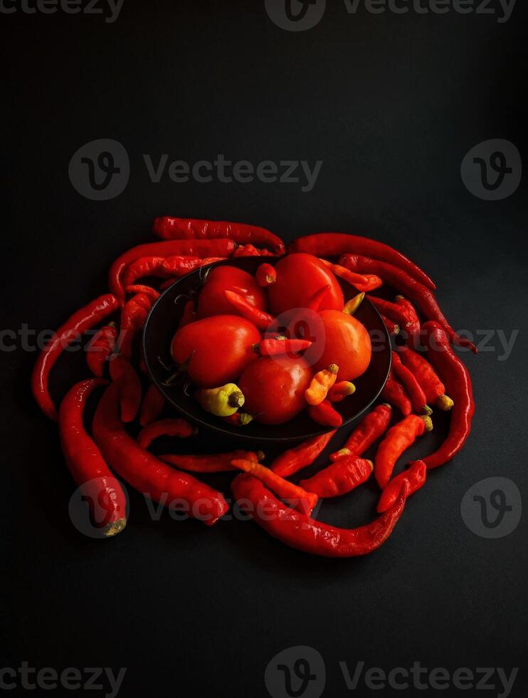 A bowl of red peppers and tomatoes on a black background photo