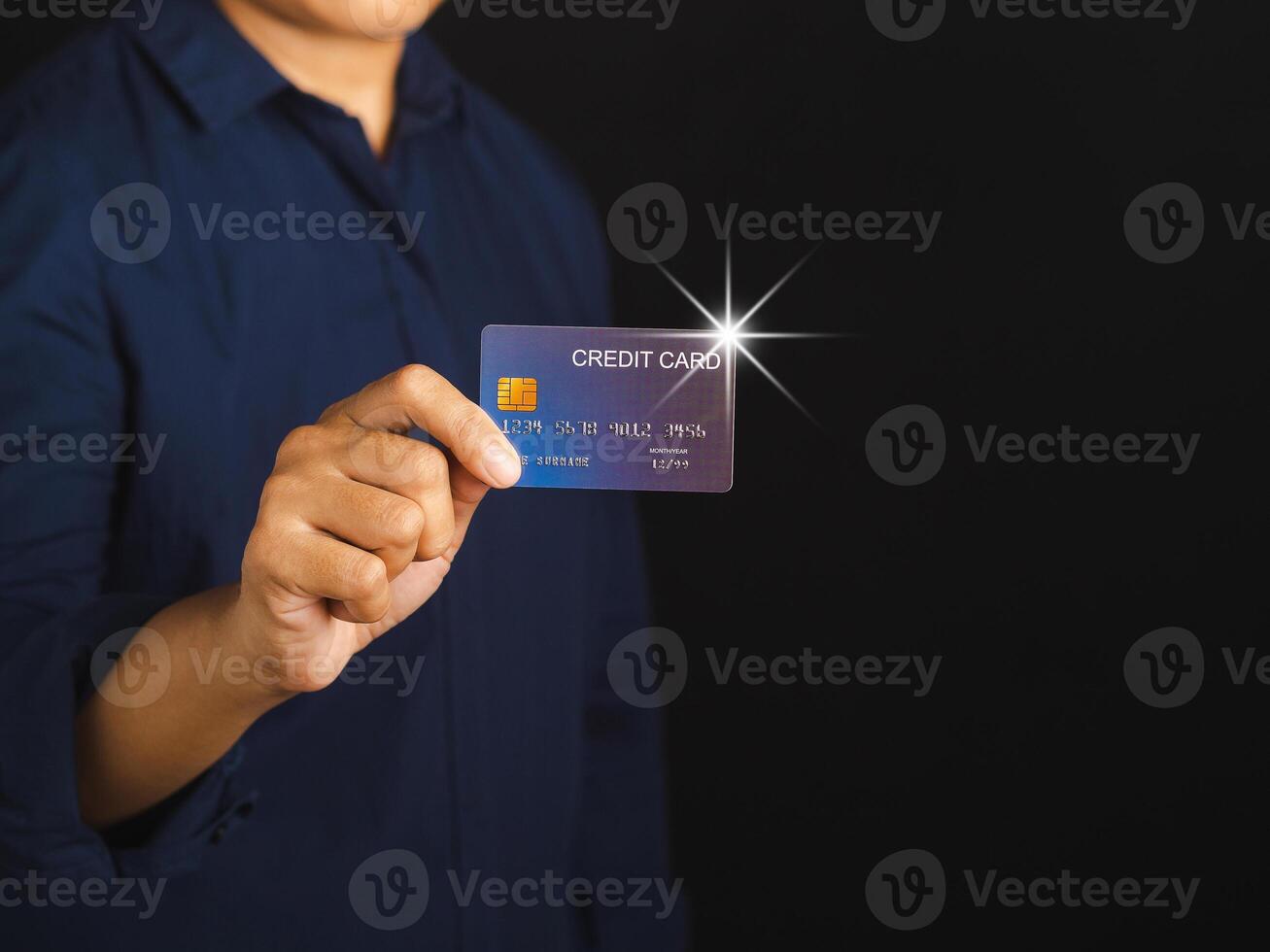 Midsection of a businessman in a blue shirt holding a mockup blue credit card while standing with a black background in the studio. Close-up photo. Space for text. Money and business concept photo