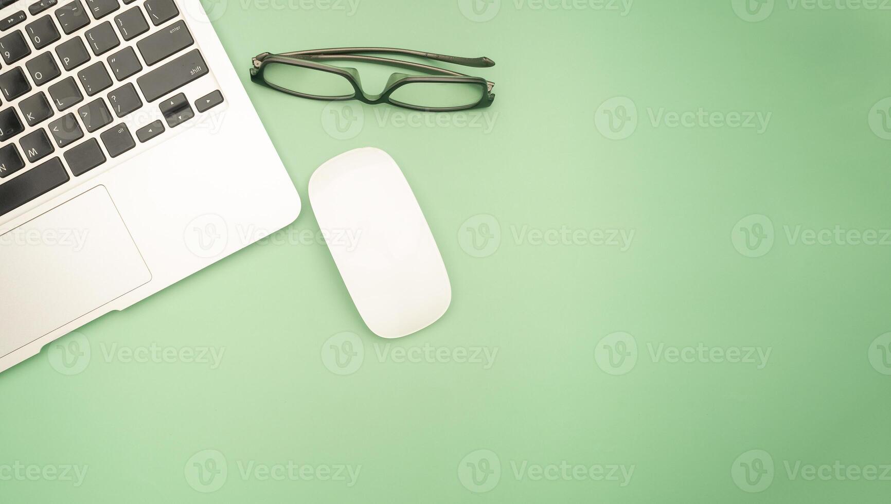 Top view of a laptop, mouse, and glasses isolated on a green background with space for text. Technology and working desk table concept photo
