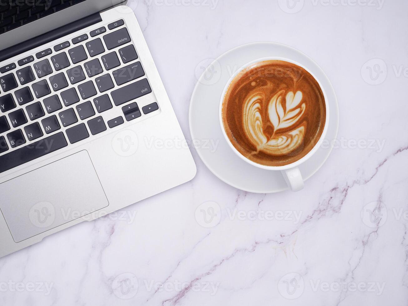 Top view of a laptop and a white coffee cup on a marble table with copy space for text. Technology and beverage concept photo