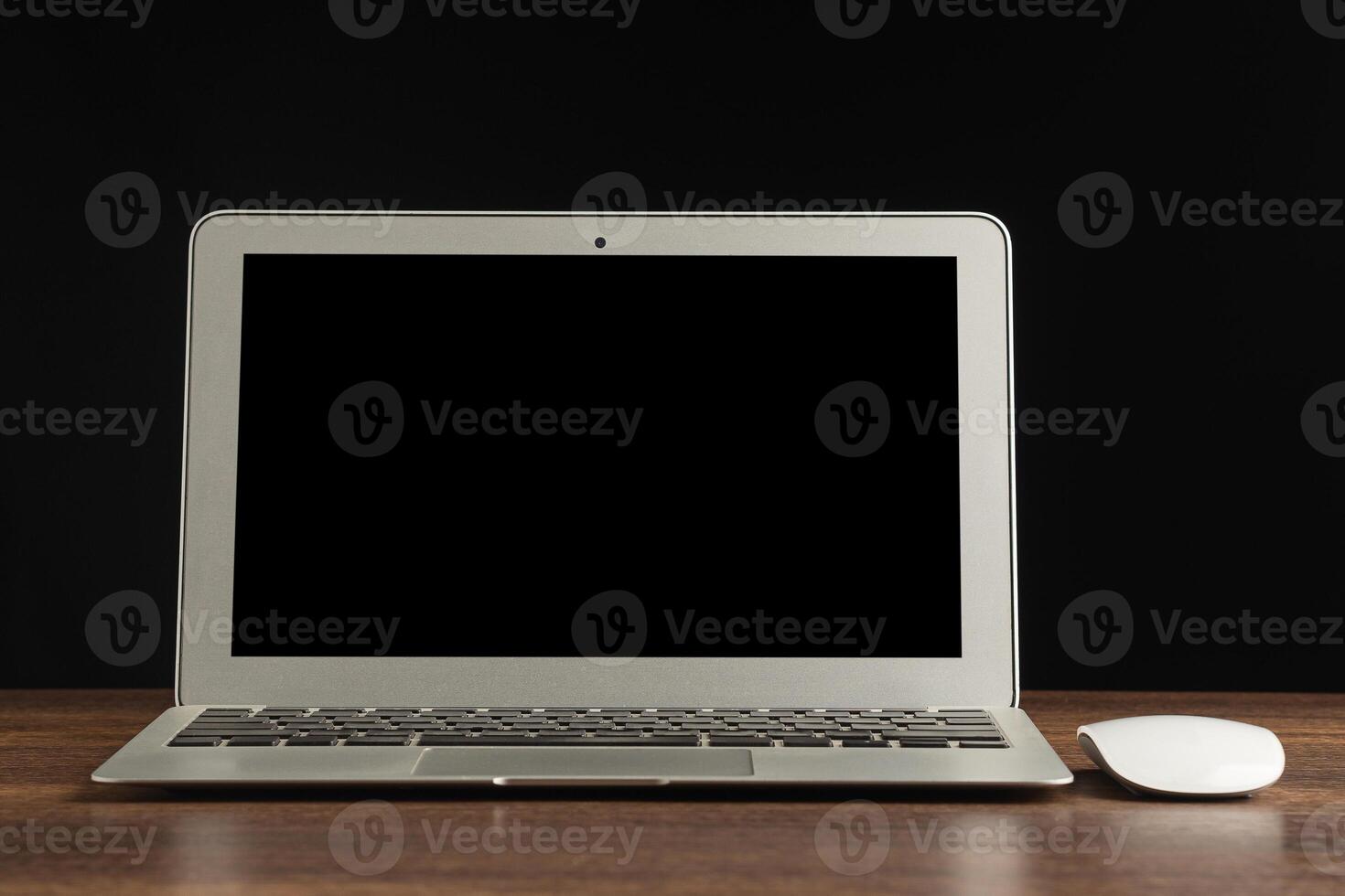 Laptop with blank screen and mouse on a wooden table with a black background. Space for text. Computer and technology concept photo