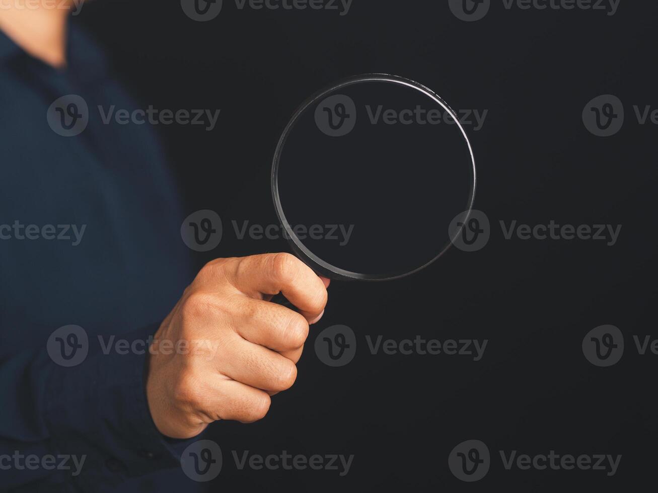 Businessman holding a magnifying glass while standing on a black background with copy space for text. Search engine optimization. Business and technology concept photo