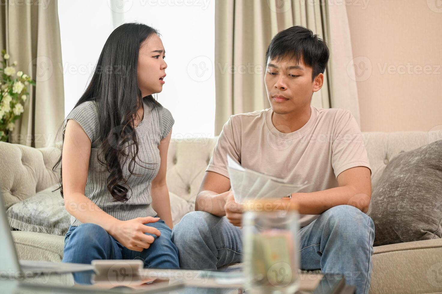 An unhappy and stressed Asian wife is arguing with her husband about unexpected expenses on the sofa photo
