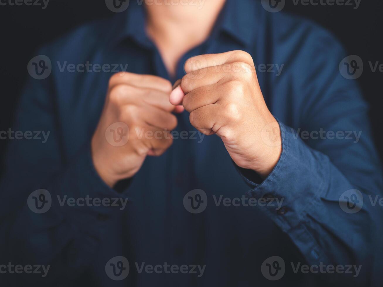 A businessman in a blue shirt raised his fist air while standing with a black background in the studio. Space for text. Concept of victory, success, and winning photo