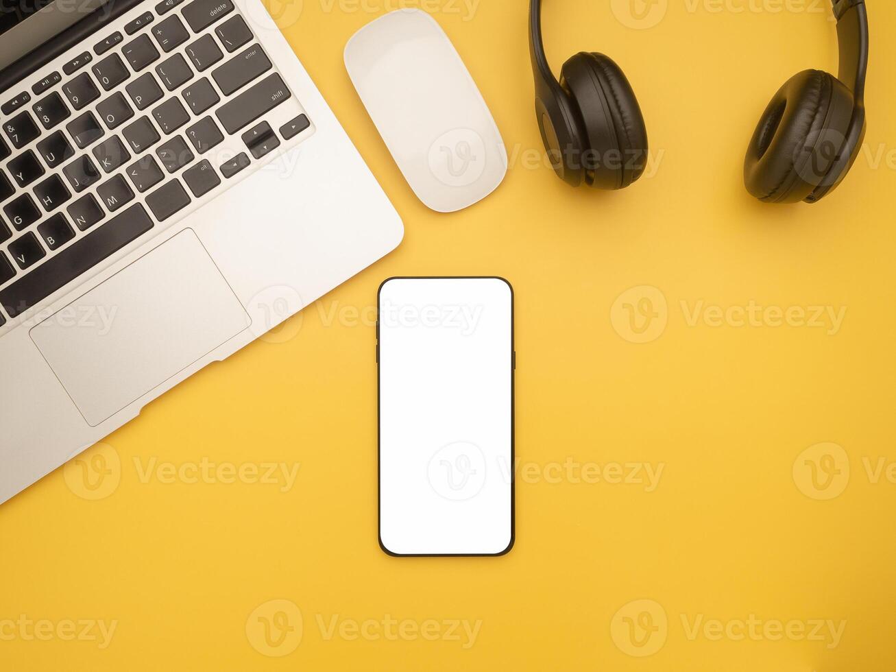 Top view of a laptop, mouse, headphones, and a smartphone isolated on a yellow background with copy space for text. Flat lay. Working desk table and relaxation concept photo