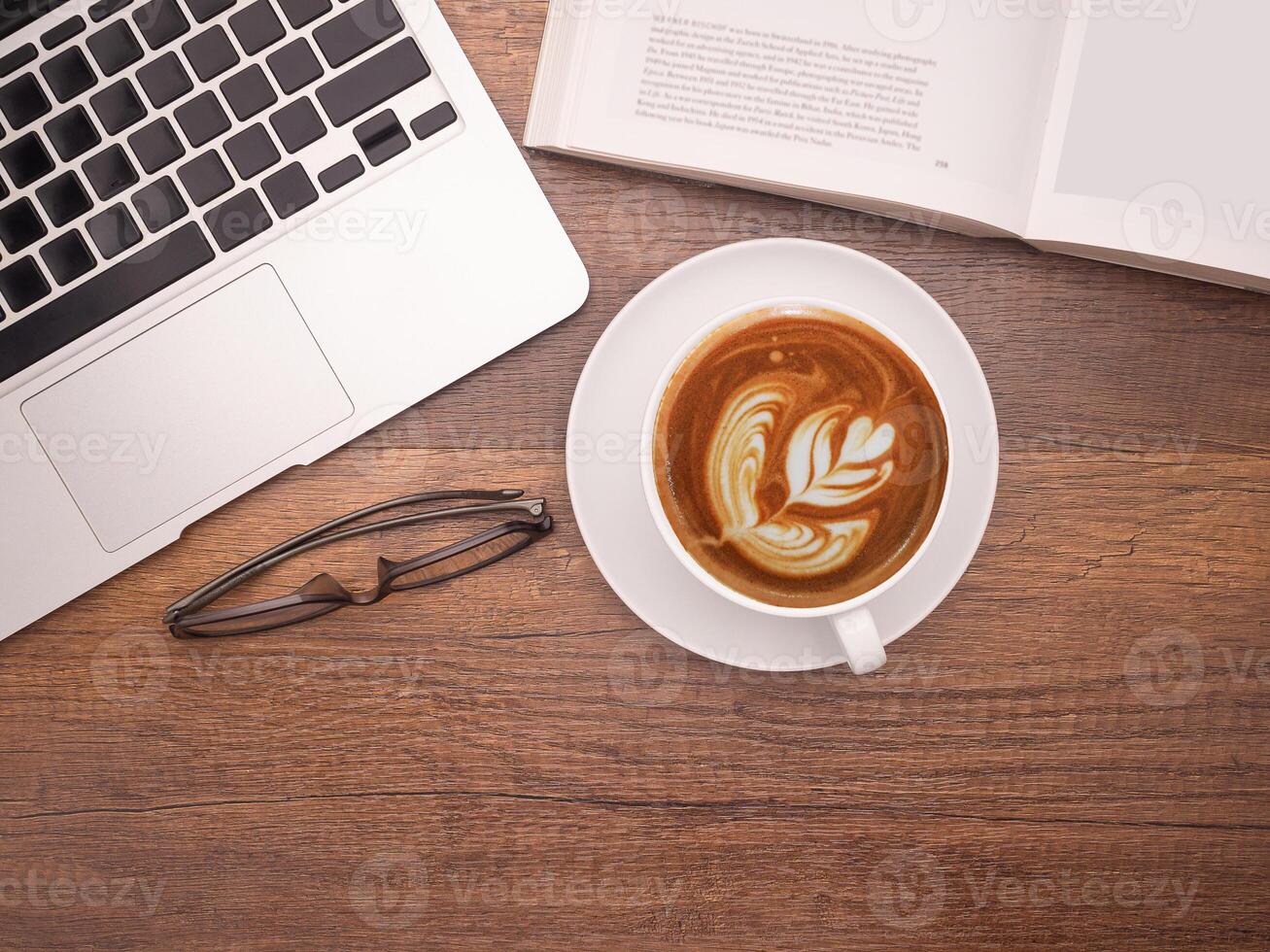 Top view of a laptop, a book, glasses, and a coffee cup on a wooden table in the office. Flat lay, space for text. Working desk table concept photo