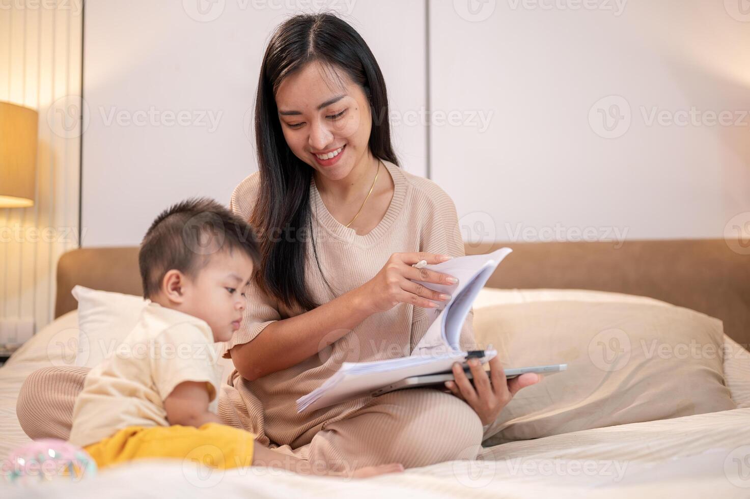 A caring Asian mom is taking care of her cute little son in bed while working remotely at home. photo