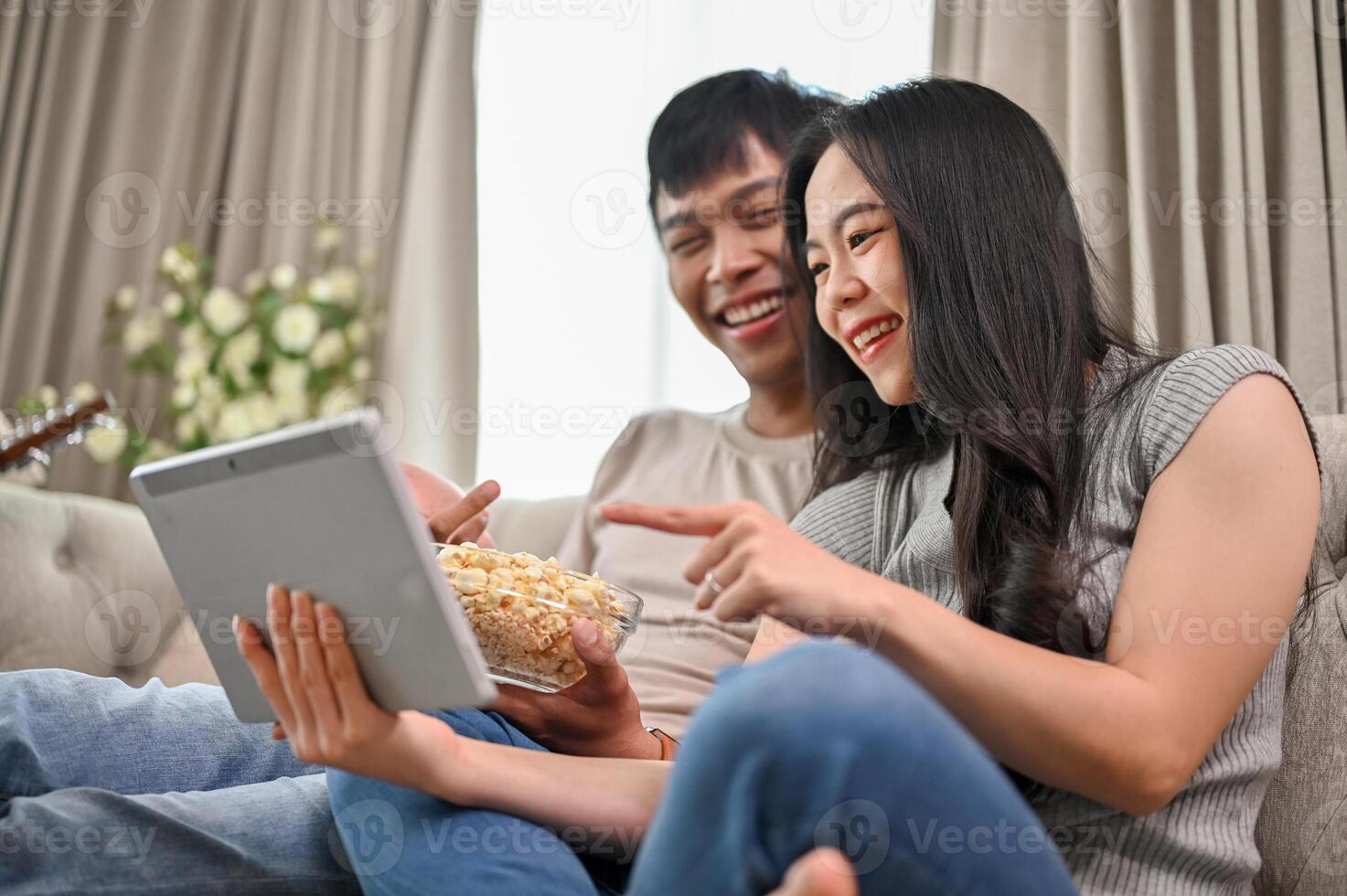 Happy Asian couple watching a movie on a digital tablet while relaxing on a sofa at home together. photo