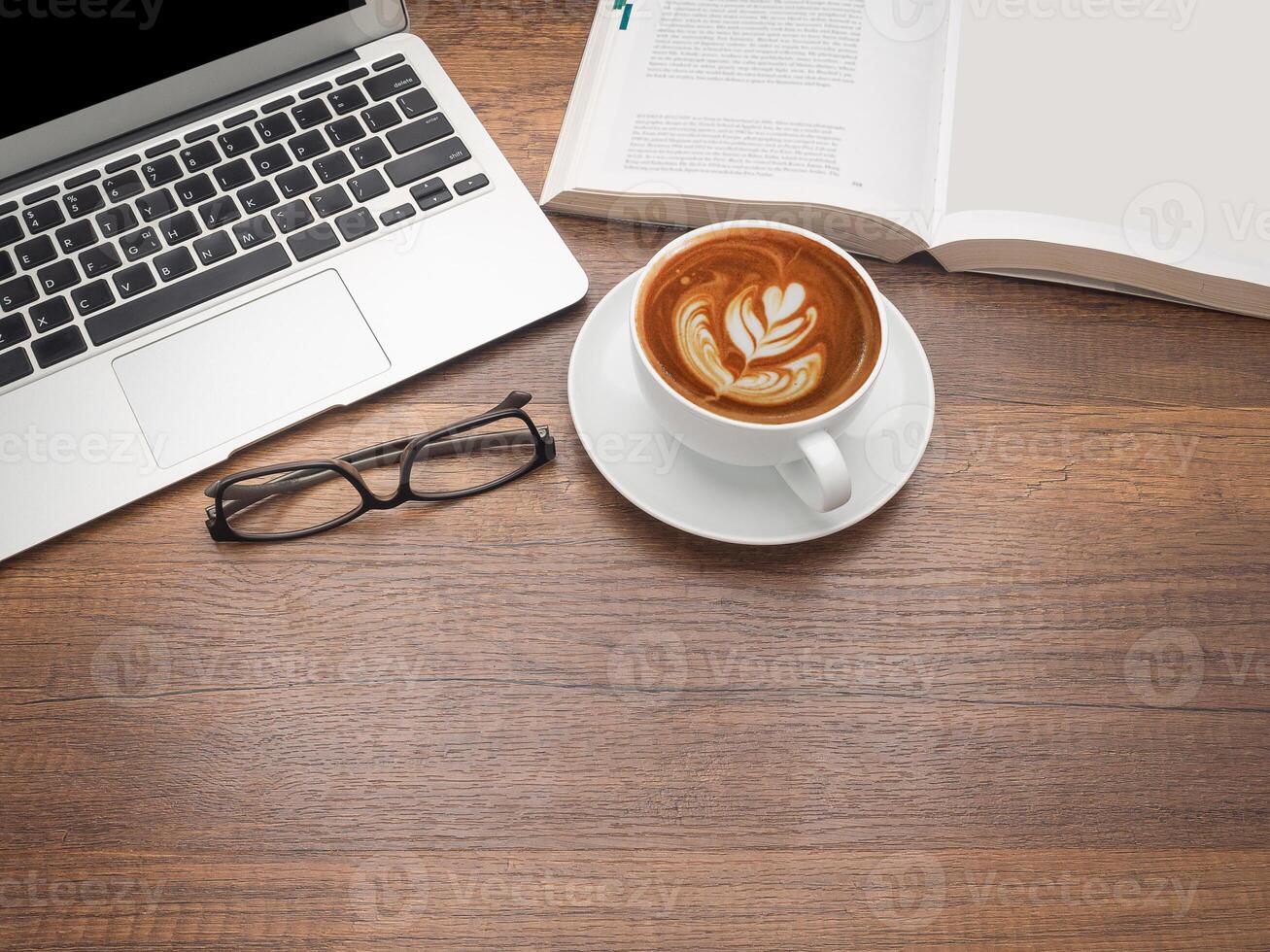 Working table concept. Top view of a laptop, a book, glasses, and a coffee cup on a wooden table in the office. Flat lay, space for text photo