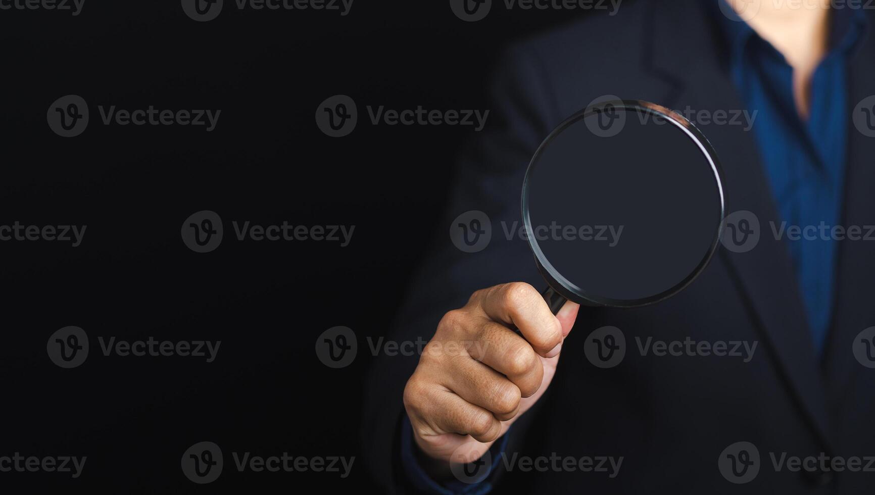 Businessman holding a magnifying glass while standing on a black background with copy space for text. Search engine optimization. Business and technology concept photo