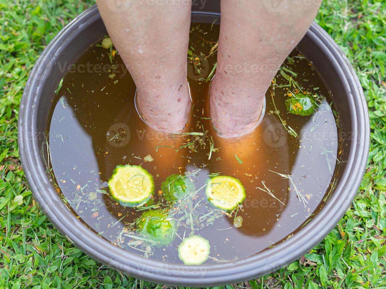 Close-up of the foot spa with herbs water for relaxation treatment. A senior woman who has ankle pain uses herbal treats to relax the muscles by soaking warm water that boiled from herbs photo