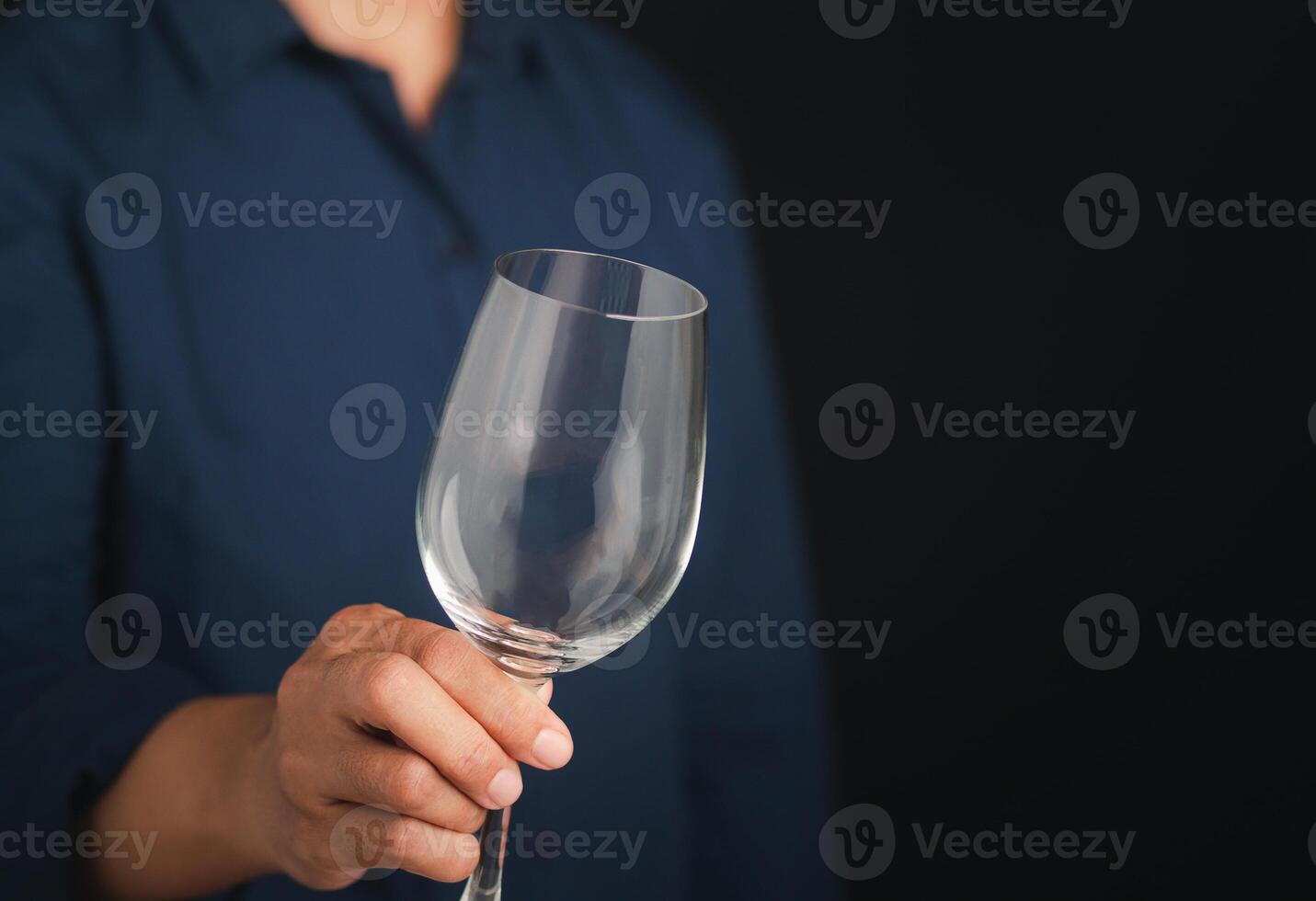 Midsection of a man holding an empty glass of wine while standing with a black background. Space for text photo