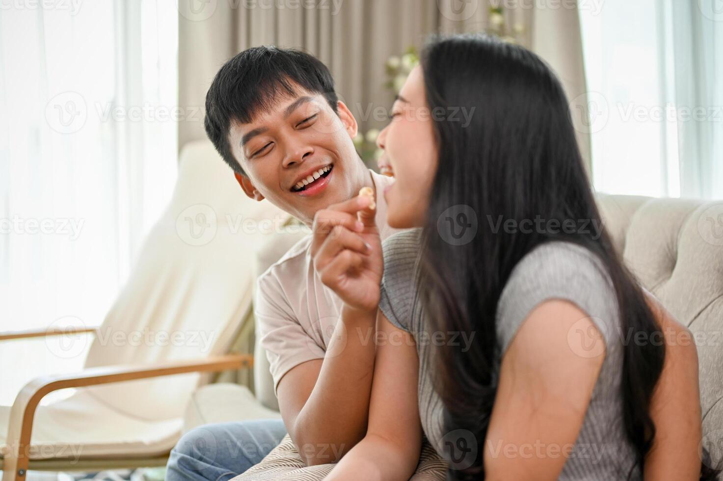 Happy, lovely young Asian couple enjoy eating popcorn on a sofa in the living room. photo