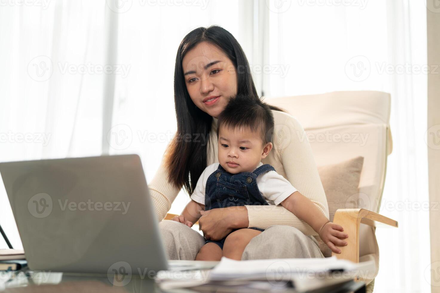 A beautiful Asian businesswoman mom is working remotely at home while taking care of her little son. photo