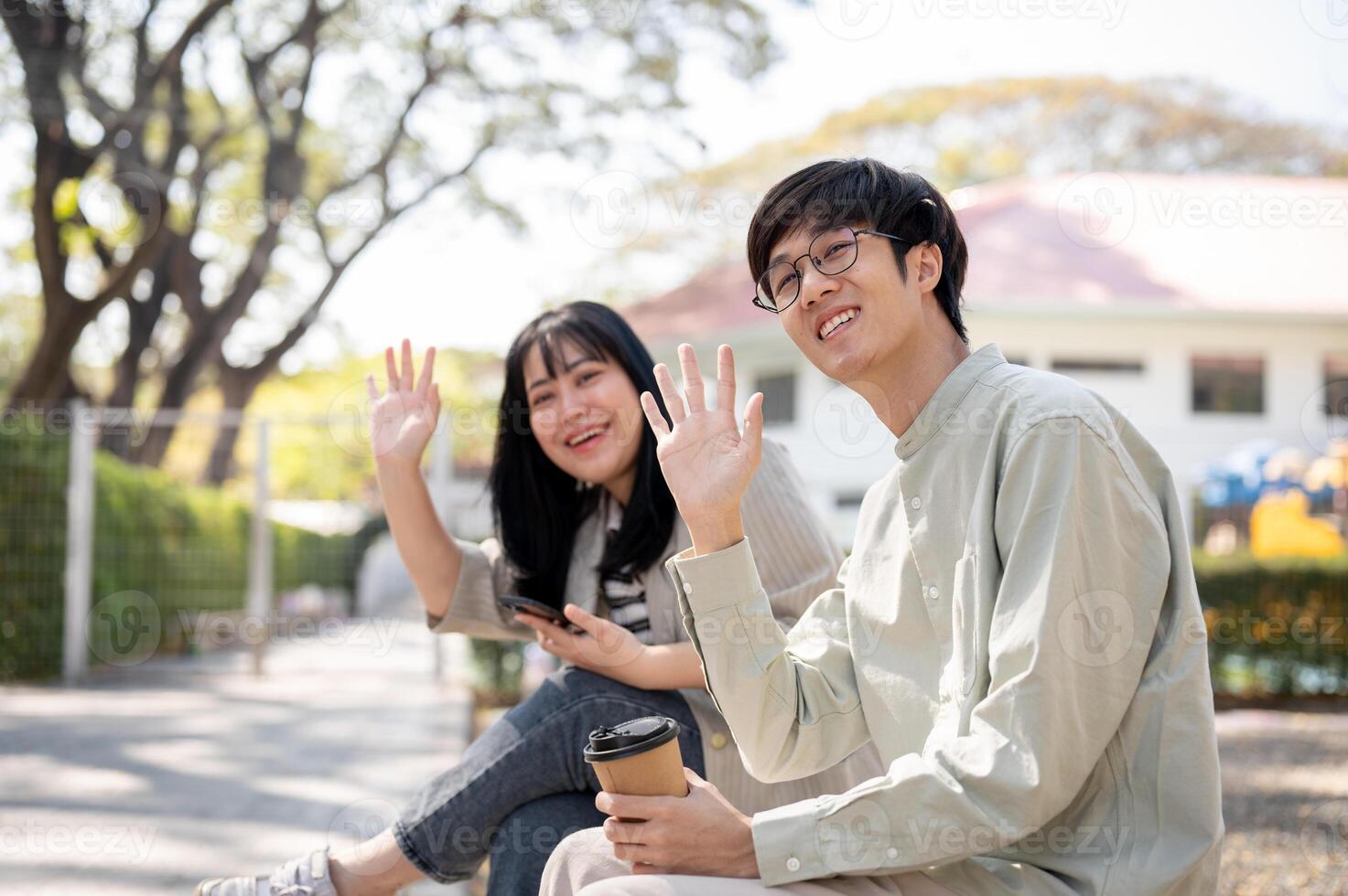 Two friendly friends are waving their hands to say hi to their friends while chilling in a park. photo