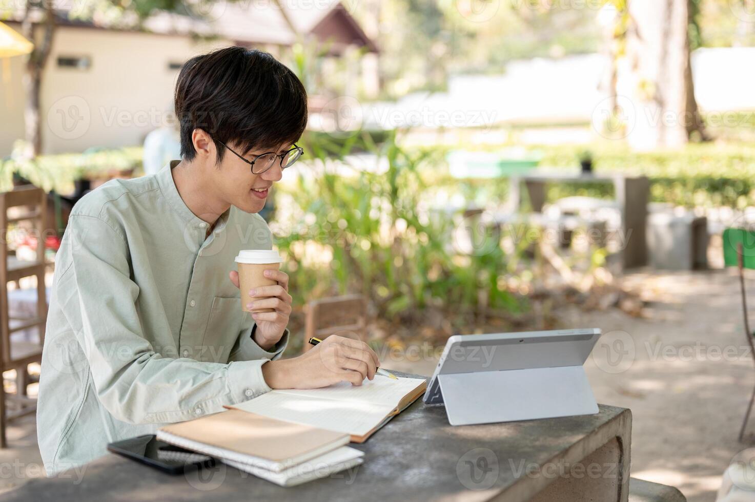 A positive and smart Asian man is working remotely at a cafe, studying online, or doing homework. photo