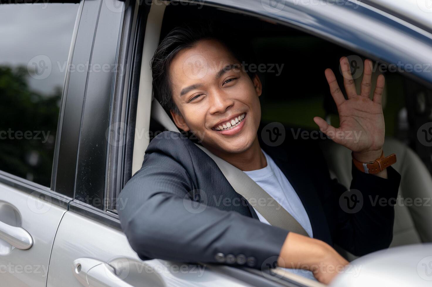 A good-looking, cheerful Asian businessman is driving a car, waving his hand and smiling. photo