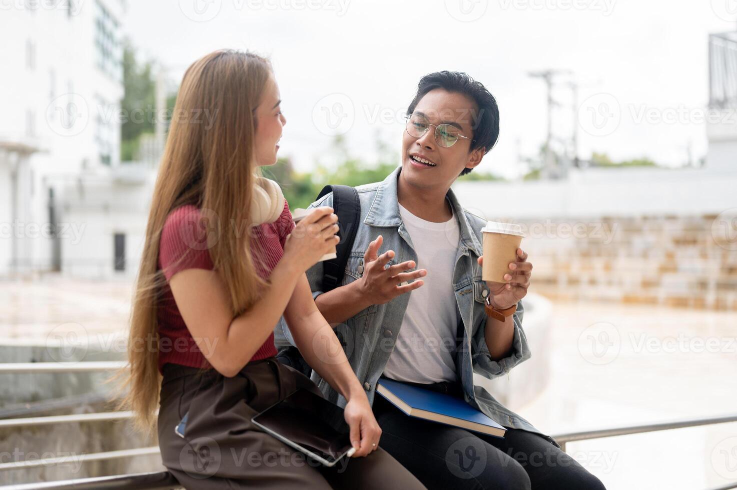 Two cheerful Asian college students are enjoying a conversation outdoors while having coffee. photo