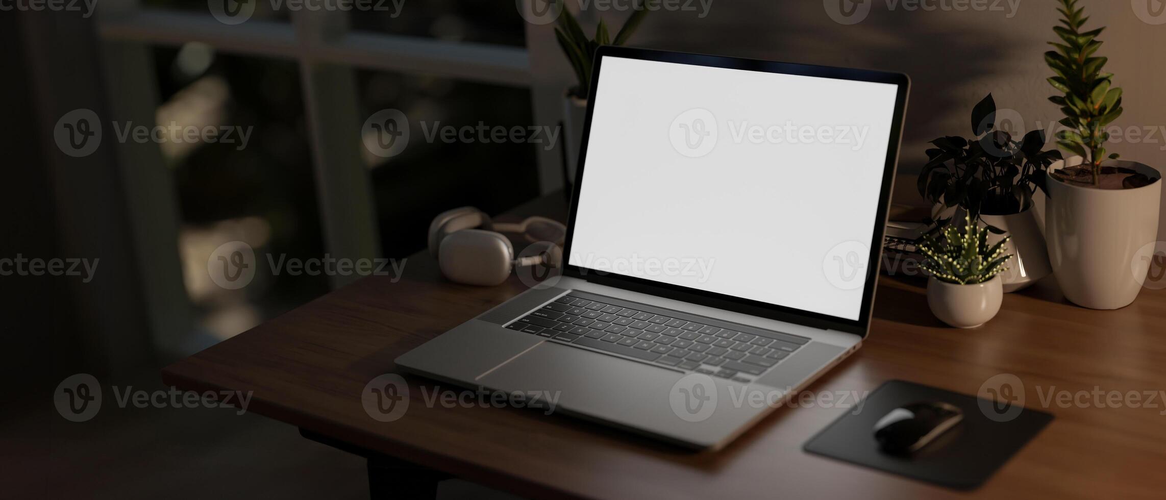 A laptop computer with a white screen mockup on a wooden table in a room at nighttime. photo
