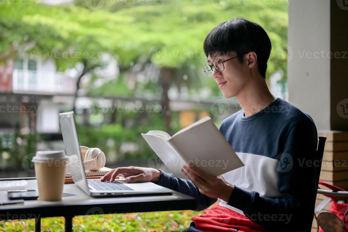 A young, positive Asian male college student is using his laptop and researching in a book. photo