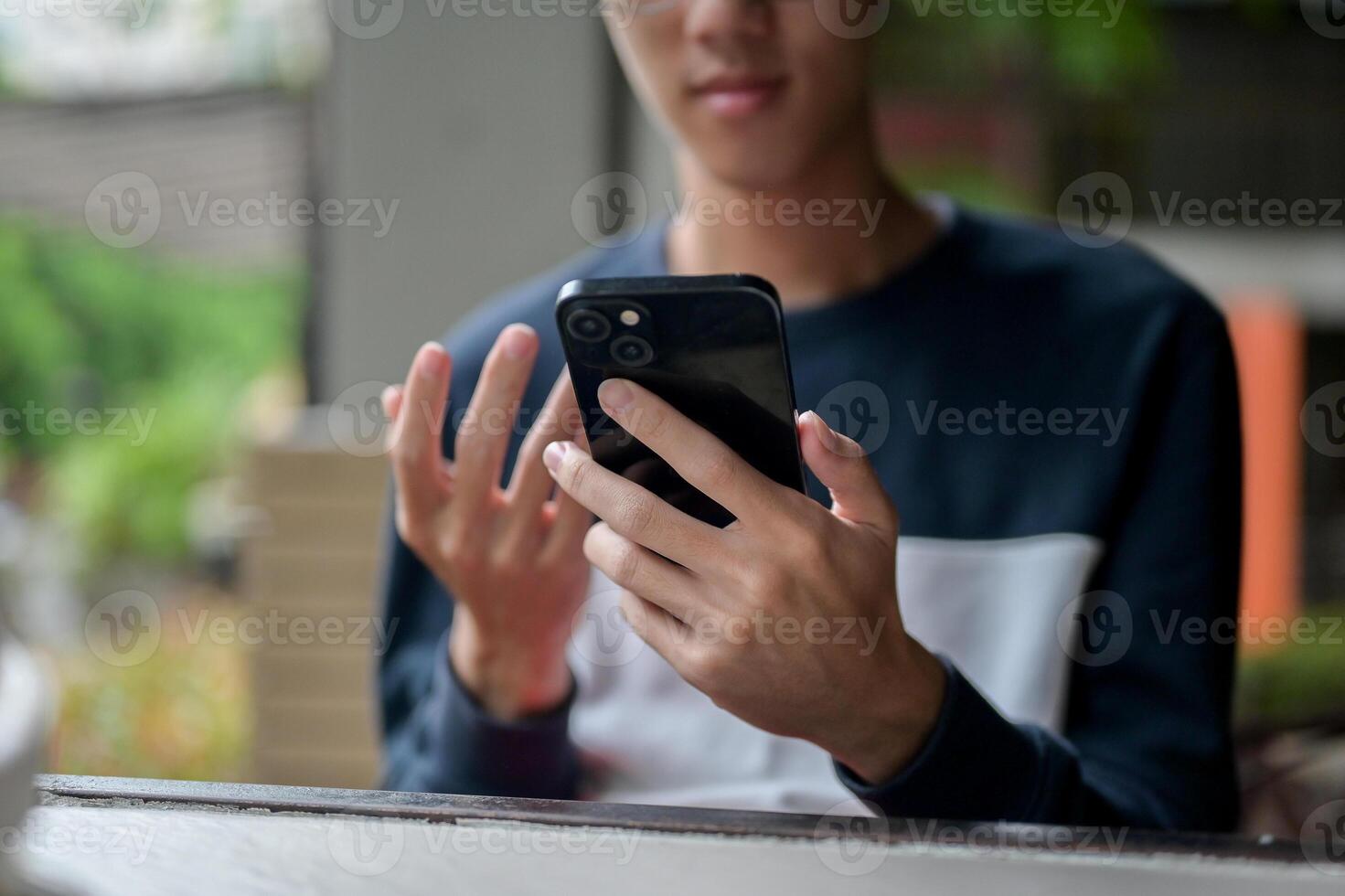 An Asian man using his smartphone while sitting at a table in a cafe. photo
