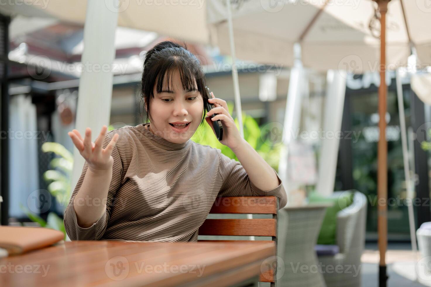 A positive woman is talking on the phone with someone while sitting at an outdoor table of a cafe. photo