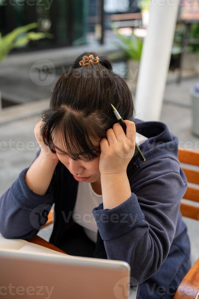 A stressed young Asian woman is feeling overworked and tired while working remotely at a cafe. photo