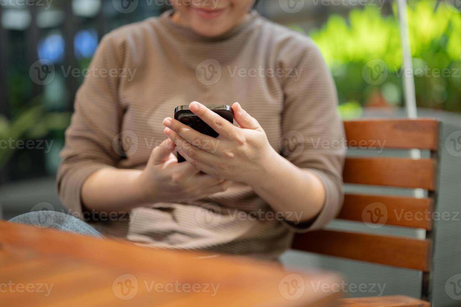 A cropped shot of a woman using her smartphone while relaxing at an outdoor table. photo