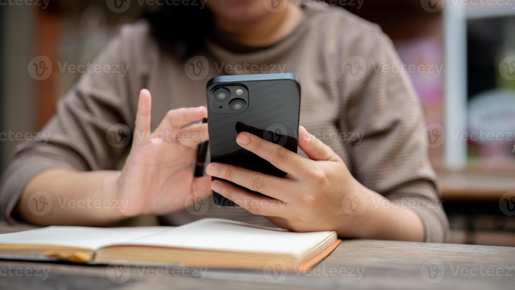 A cropped shot of an Asian woman using her smartphone while reading a book or doing some work. photo