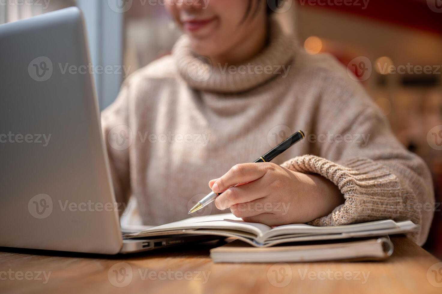 A woman in a comfy sweater is working remotely at a cafe, making list in her notebook. photo