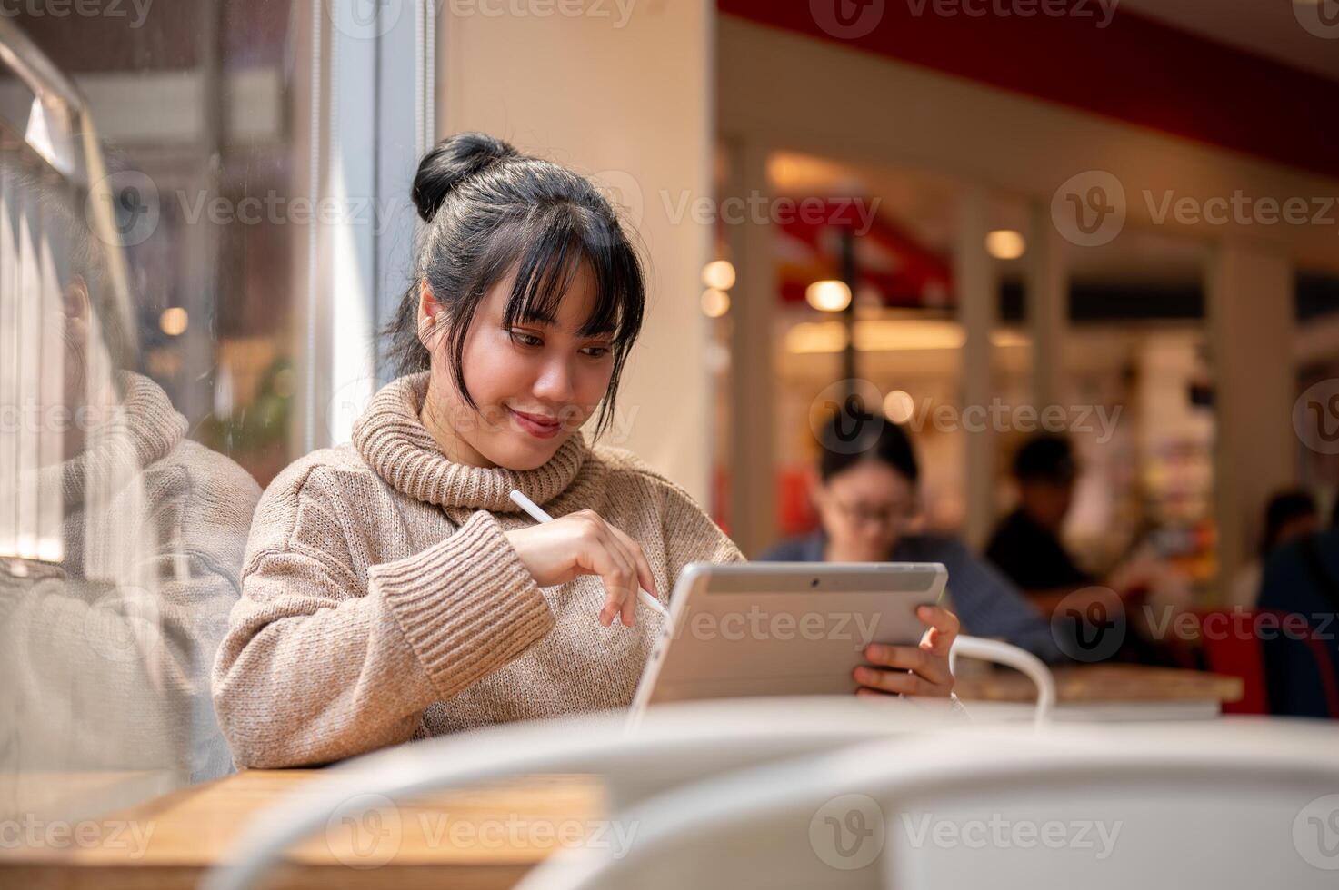 An attractive, happy Asian female is working remotely at a cafe co-working space, using her tablet. photo