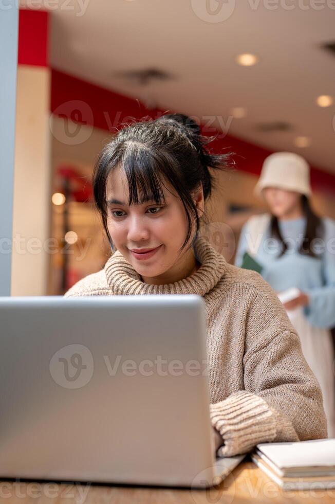 An attractive Asian woman in a comfy sweater is working remote at a cafe, working on her laptop. photo