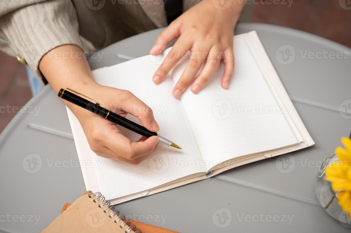 A close-up shot of a businesswoman writing something in her book, working remotely at a cafe. photo