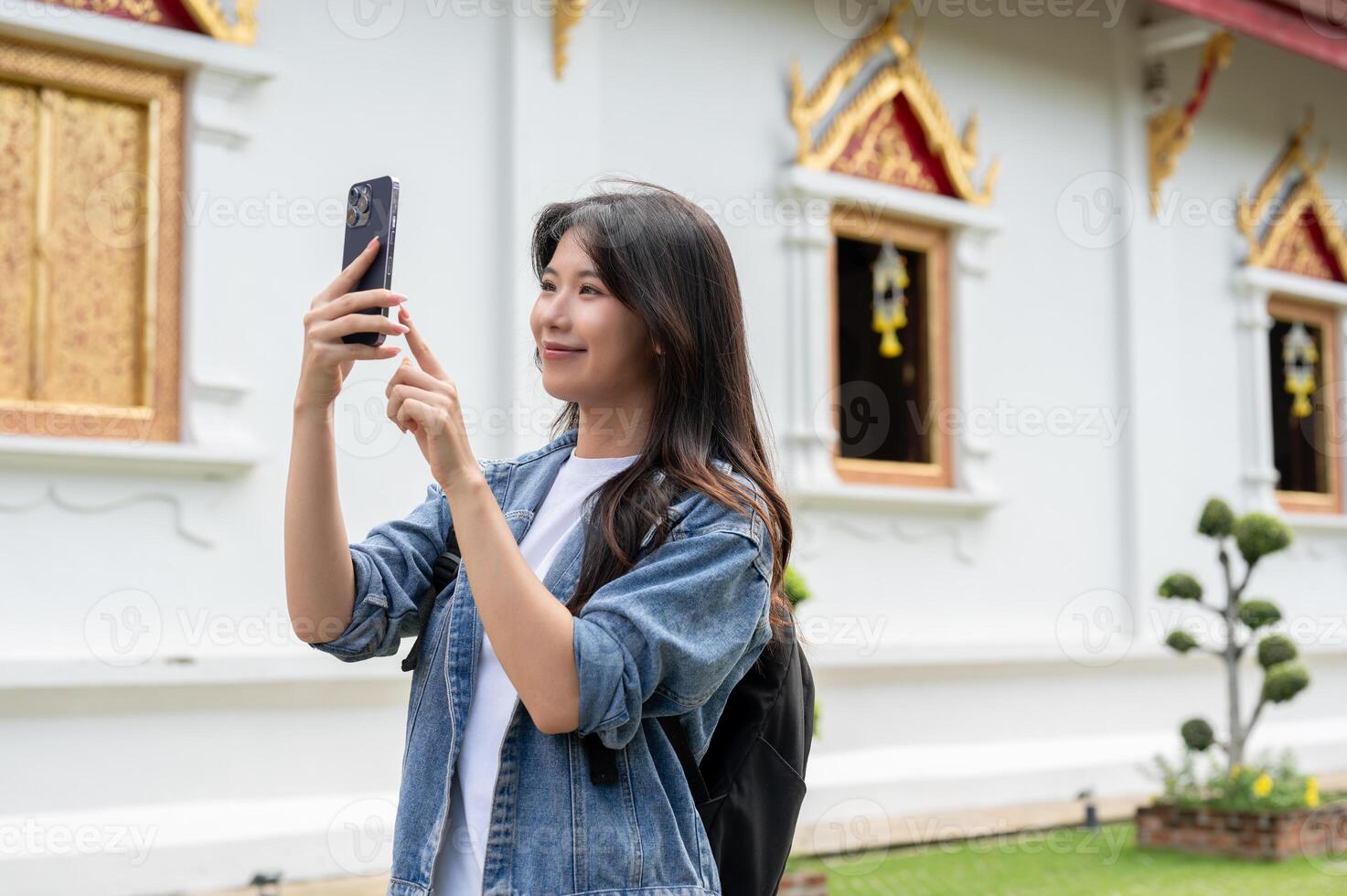 A happy Asian female traveler is taking a picture of a Thai temple with her smartphone. photo