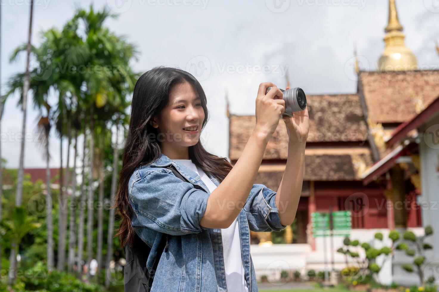 A pretty and positive Asian female tourist is taking a photo of a beautiful temple with her camera.