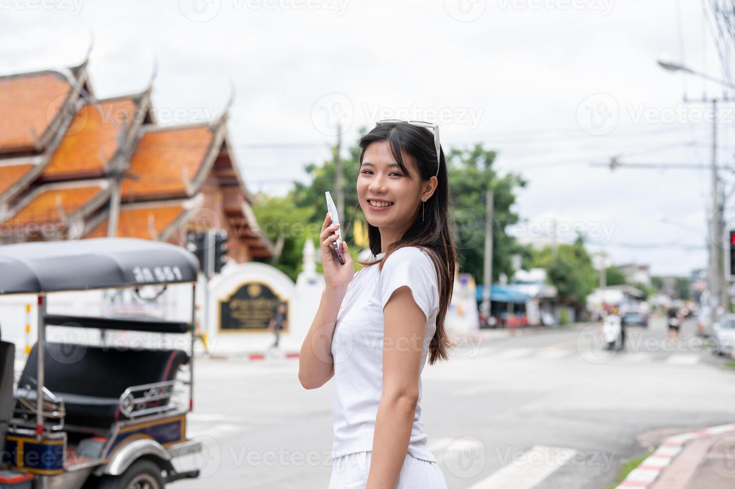 A positive Asian woman is talking on the phone while standing by the street, smiling at the camera. photo