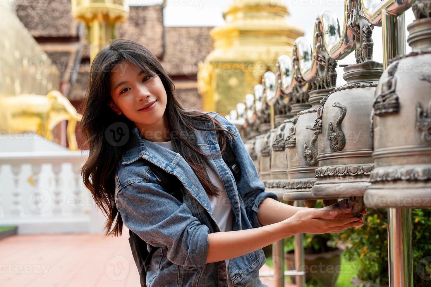 A happy Asian female tourist touching an ancient bell in a Thai temple during her visit to Thailand. photo