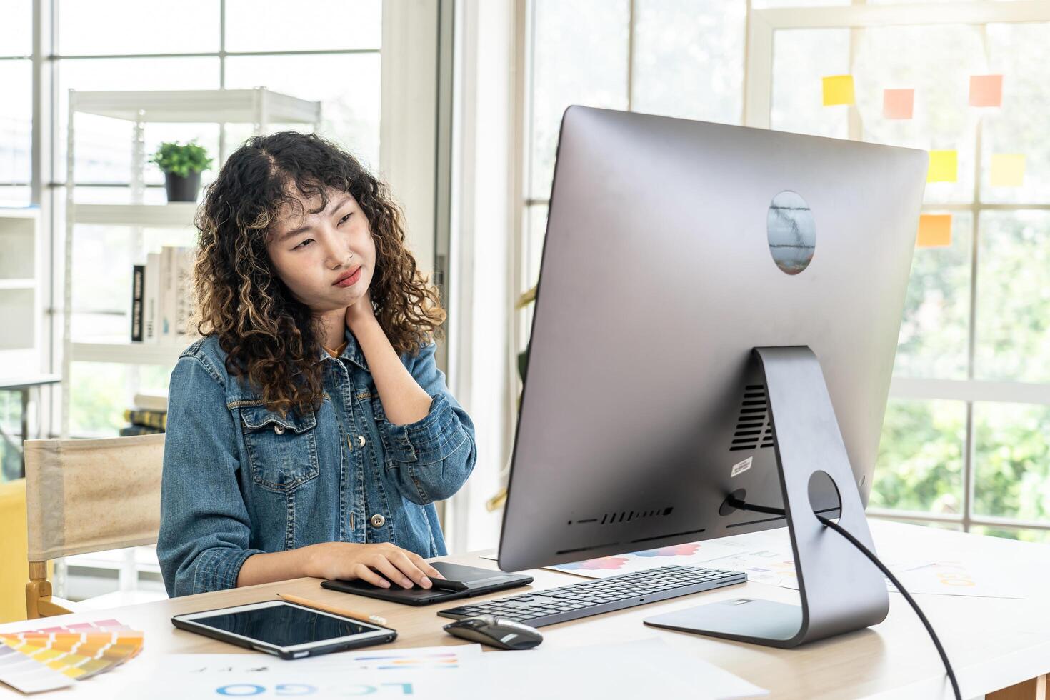Tired fatigued asian girl feel neck discomfort with computer work in office, Young Asia girl development programmer overworked tired painful shoulder neck muscle from office syndrome photo