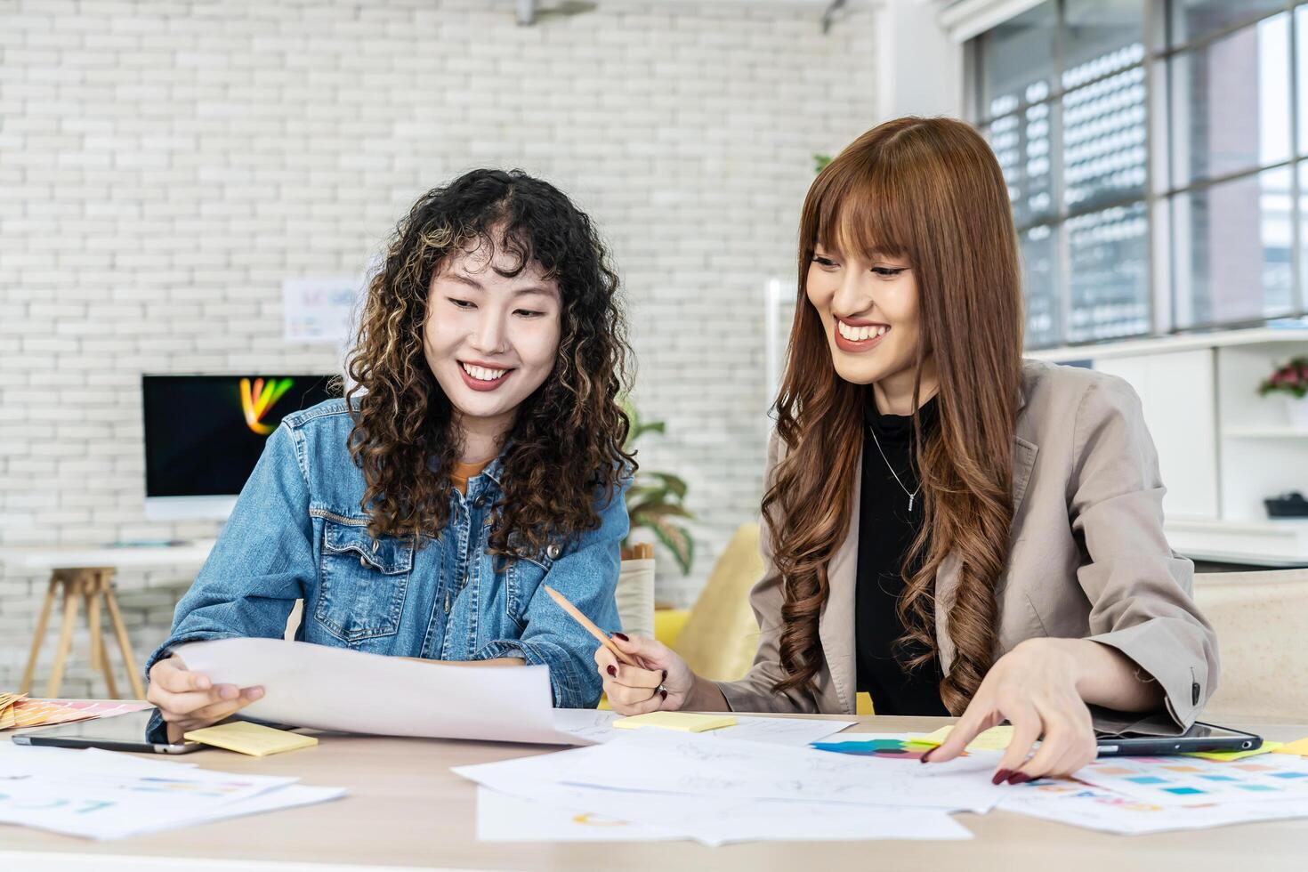 Two business young asian woman working together in office with reports and tablet, colleagues discuss financial data analyzing documents marketing project result talk business conversation photo